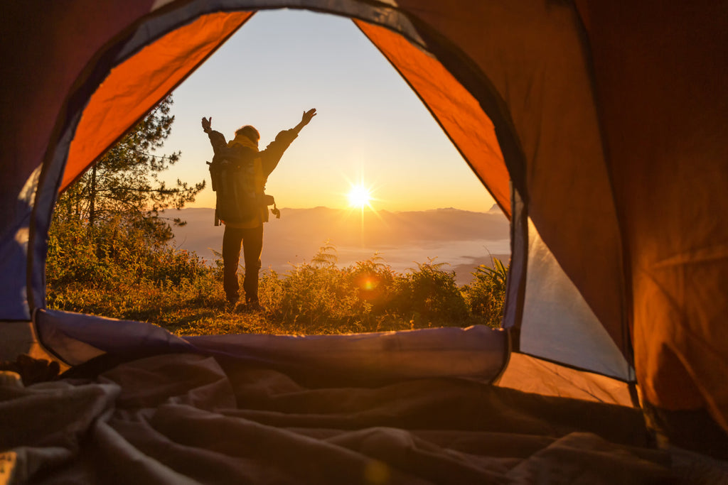 Hiker standing camping outside in sunrise mountains